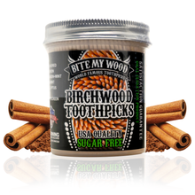 Load image into Gallery viewer, A clear plastic jar with a stainless steel screw-top lid labeled 'BITE MY WOOD Birchwood Toothpicks', containing cinnamon flavored toothpicks, alongside individual cinnamon sticks for decoration.